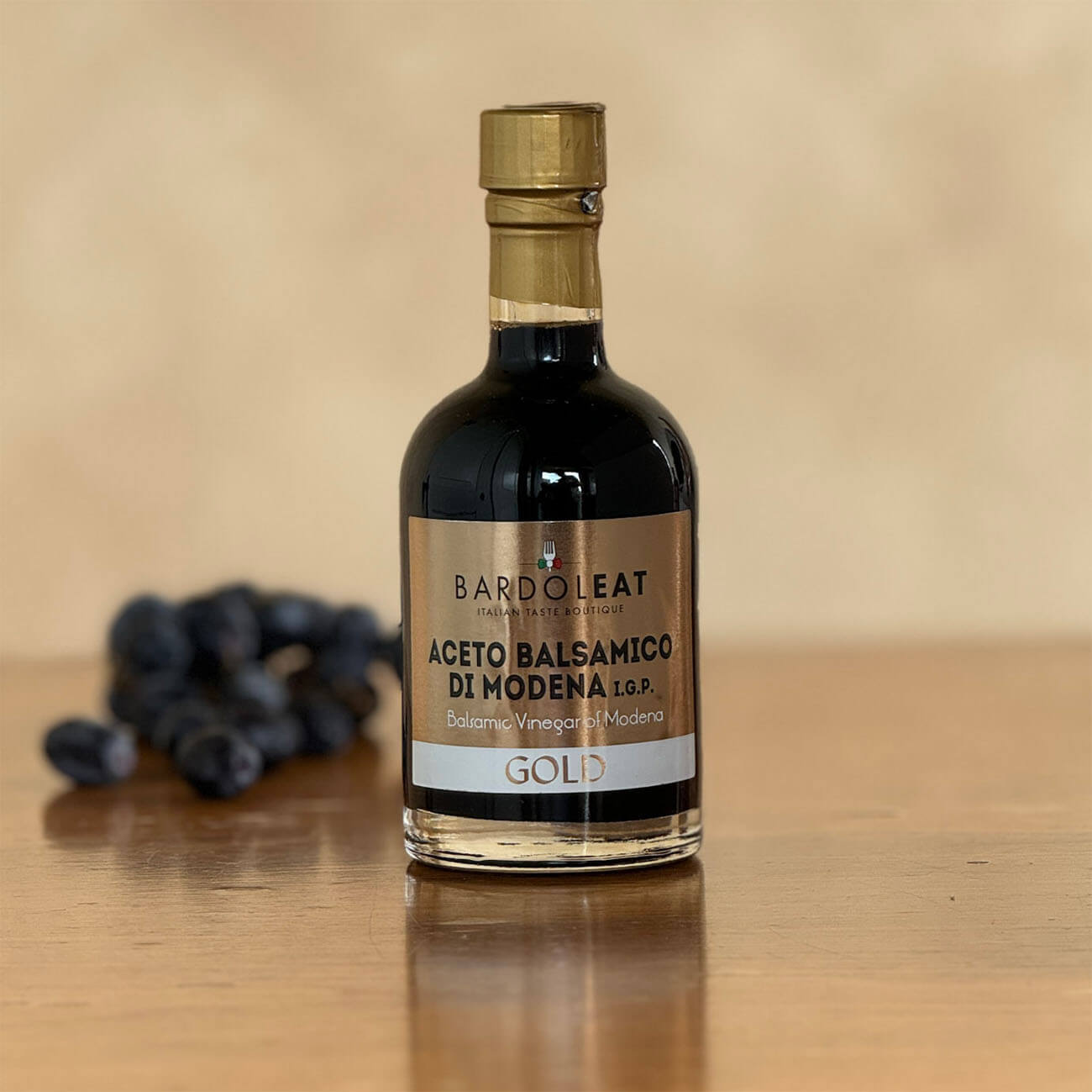 Flasche mit Aceto Balsamico di Modena Gold steht auf einem Tisch mit Weintrauben im Hintergrund