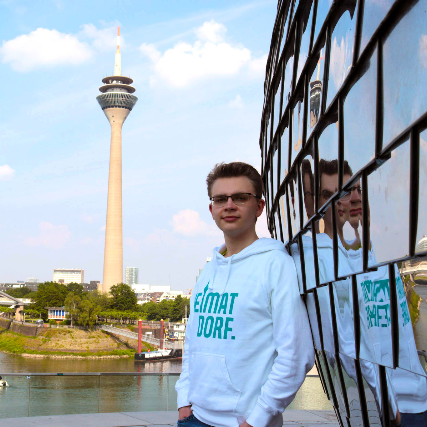 Düsseldorf Hoodie Heimatdorf in weiß mit türkisem Heimatdorf Logo vor Rheinturm im Medienhafen