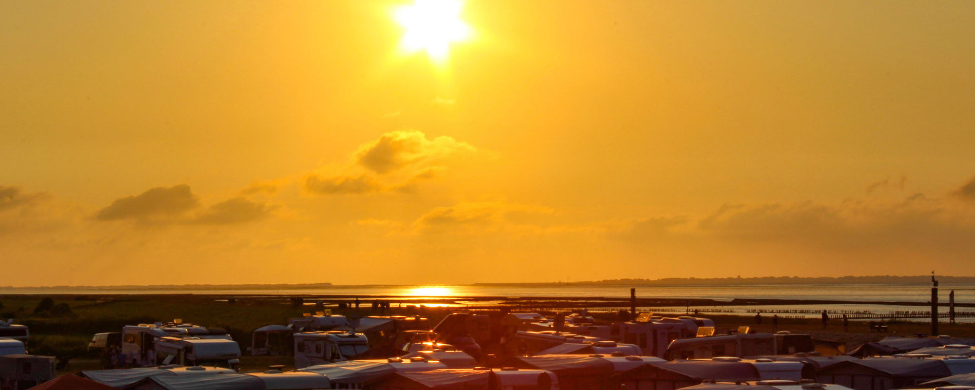 Über die Dächer von Wohnmobilen und Wohnwagen fotografierter Sonnenuntergang am Meer