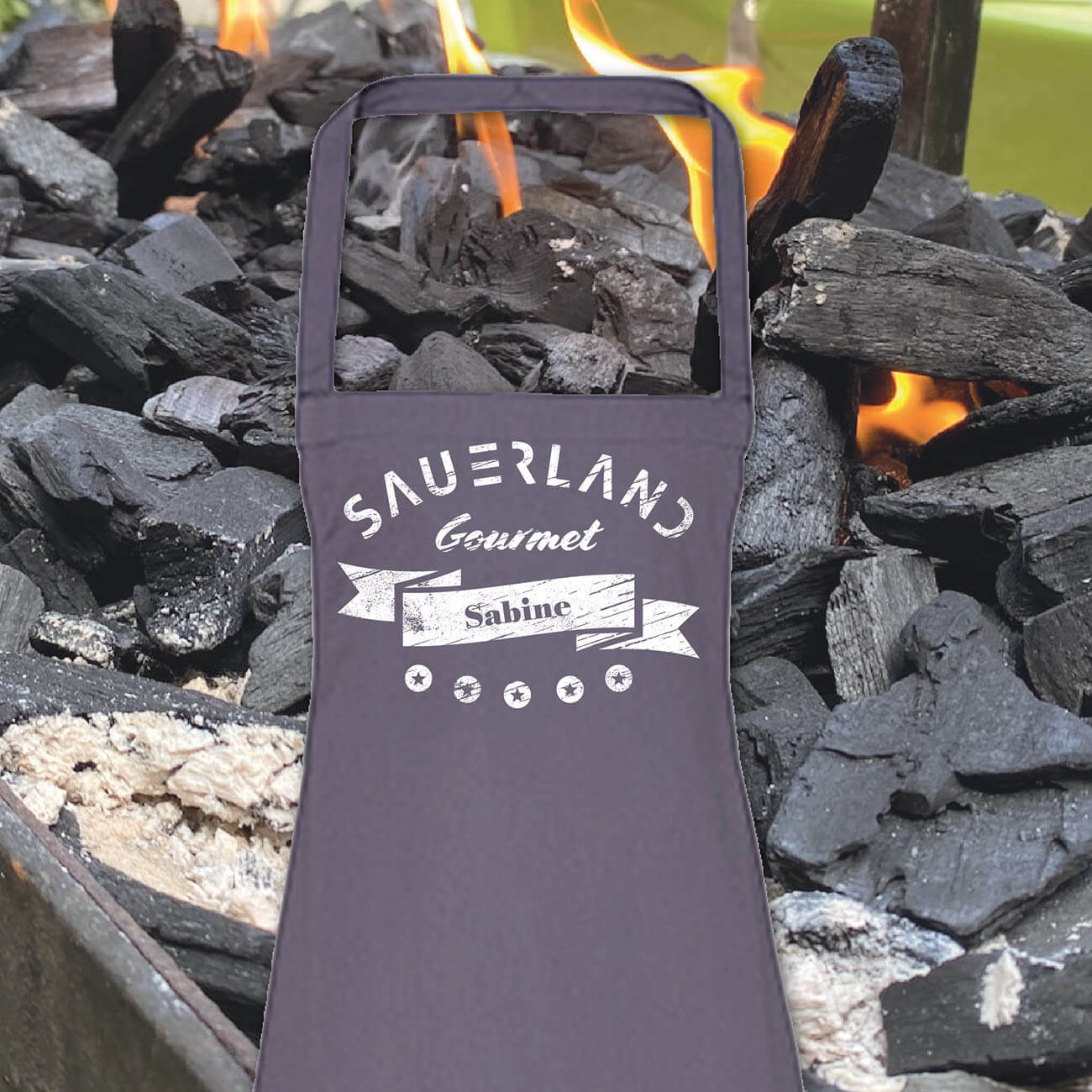 Foto einer dunkelgrauen Koch- und Grillschürze, in weiß bedruckt mit dem modernen Sauerland-Logo, dem Begriff Gourmet und einem individuellen Vornamen.