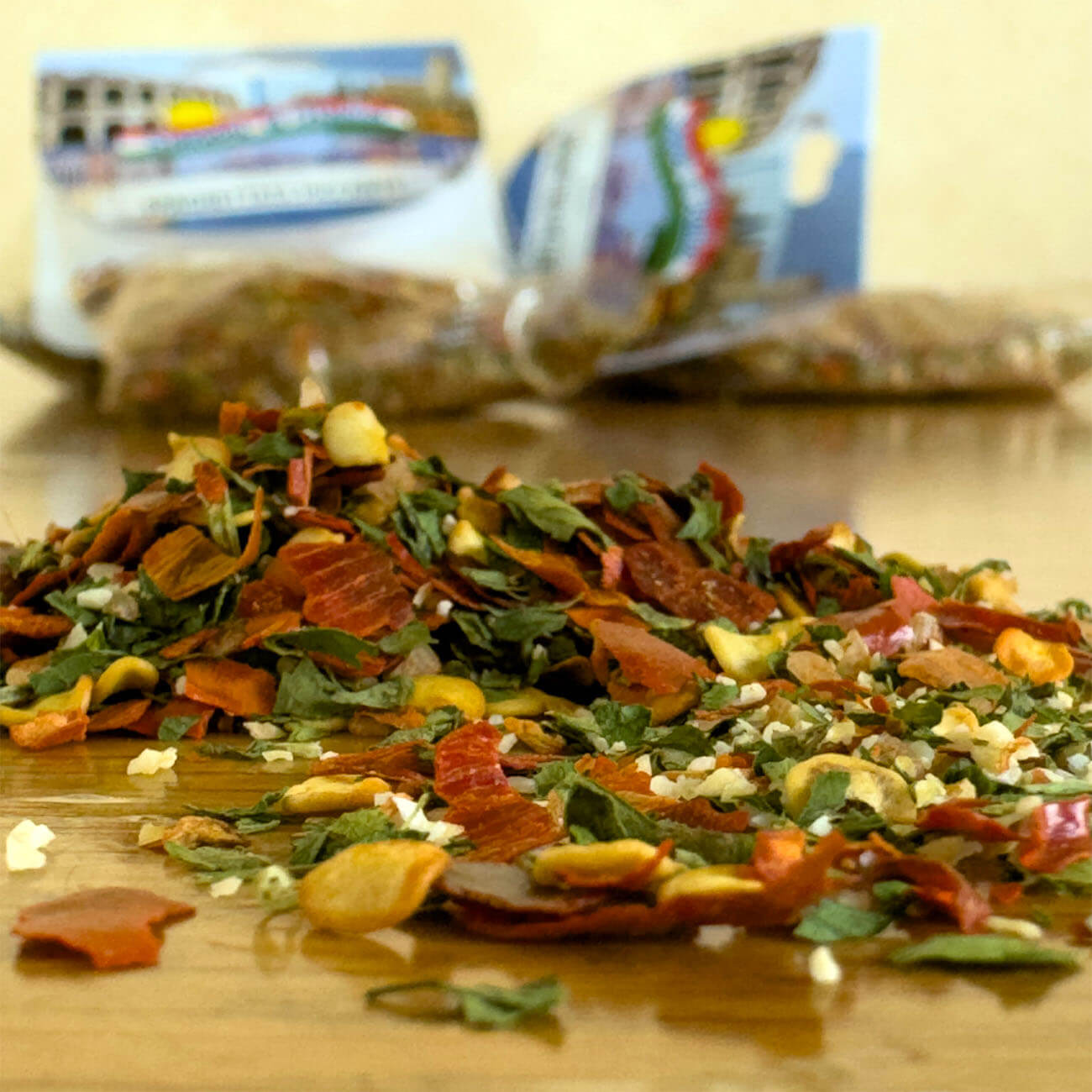 Ausgeschüttete Gewürzmischung liegt auf einem Tisch. Im Vordergrund sieht man die einzelnen Gewürze wie Chili, Petersilie und Knoblauch sowie im Hintergrund Gewürztütchen.