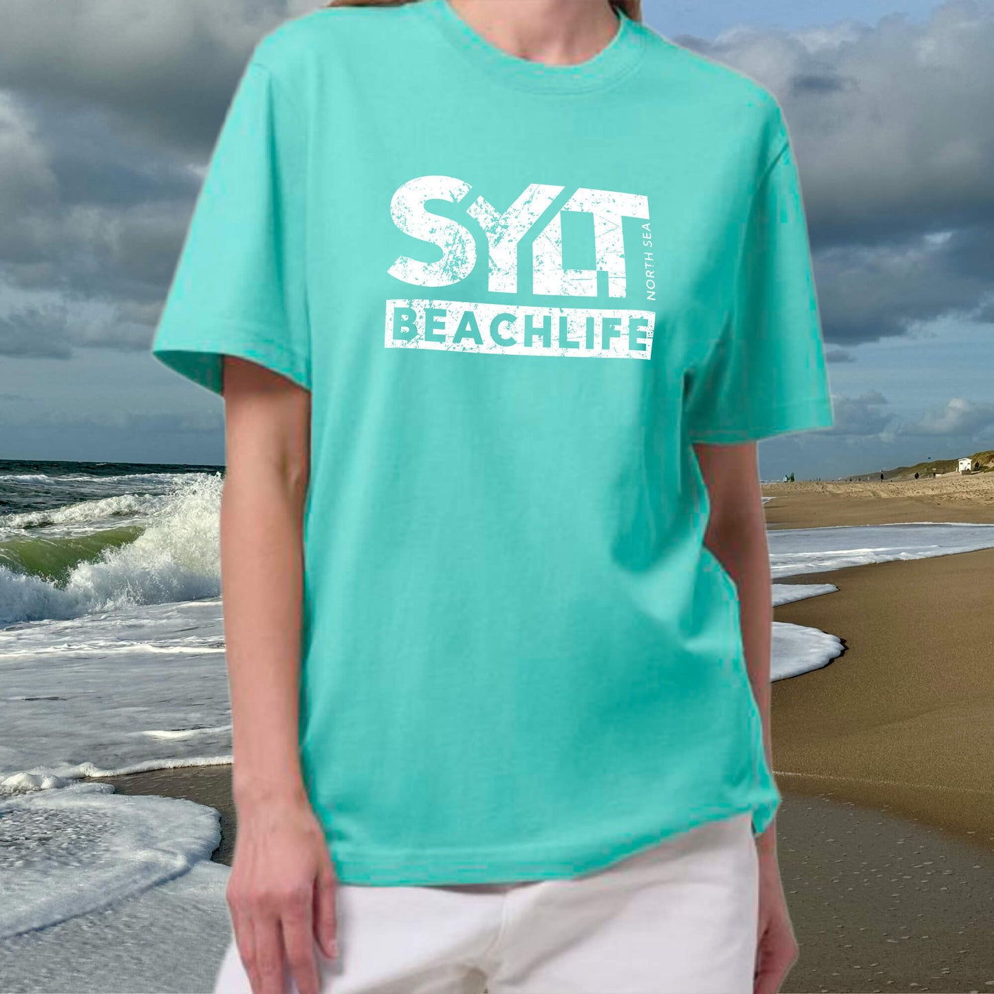 Frau trägt mint-grünes Sylt Beachlife T-Shirt aus Bio-Baumwolle am Nordseestrand mit Wellen im Hintergrund