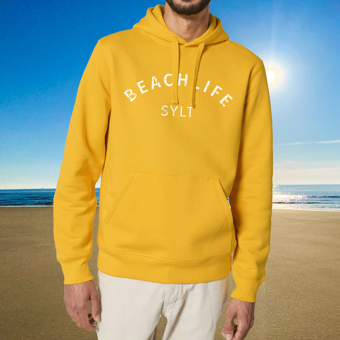 Mann steht mit sonnengelben Sylt Hoodie am Sylter Strand. Auf der Brust ist Beachlife und darunter Sylt in weiß aufgedruckt.