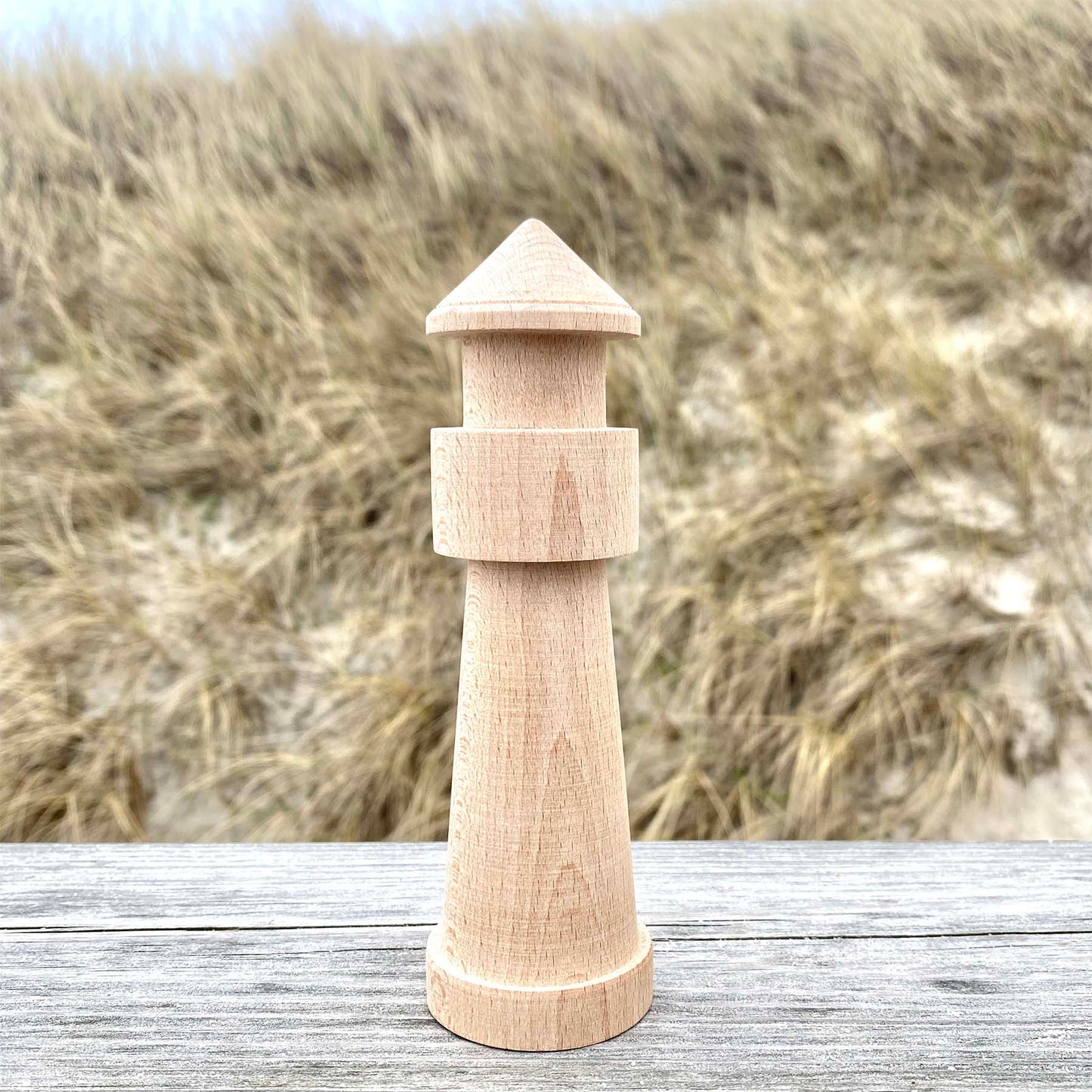 Handgedrechselter Leuchtturm aus Holz steht auf einem Holzgeländer mit Blick auf Sylter Dünen.