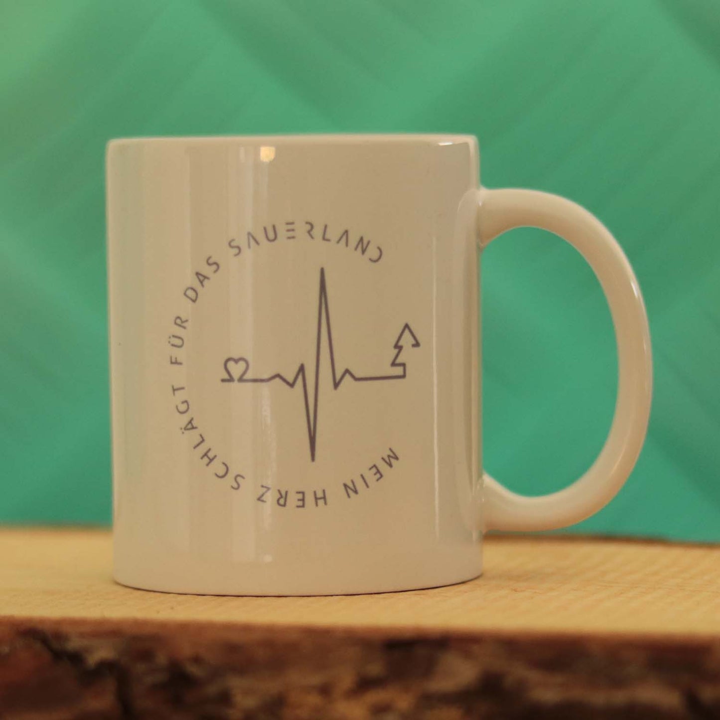 Weißer Becher mit grauem Aufdruck. Das Motiv zeigt einen Herzschlag der in einen Tannenbaum mündet und wird vom Spruch mein Herz schlägt für das Sauerland umrundet.