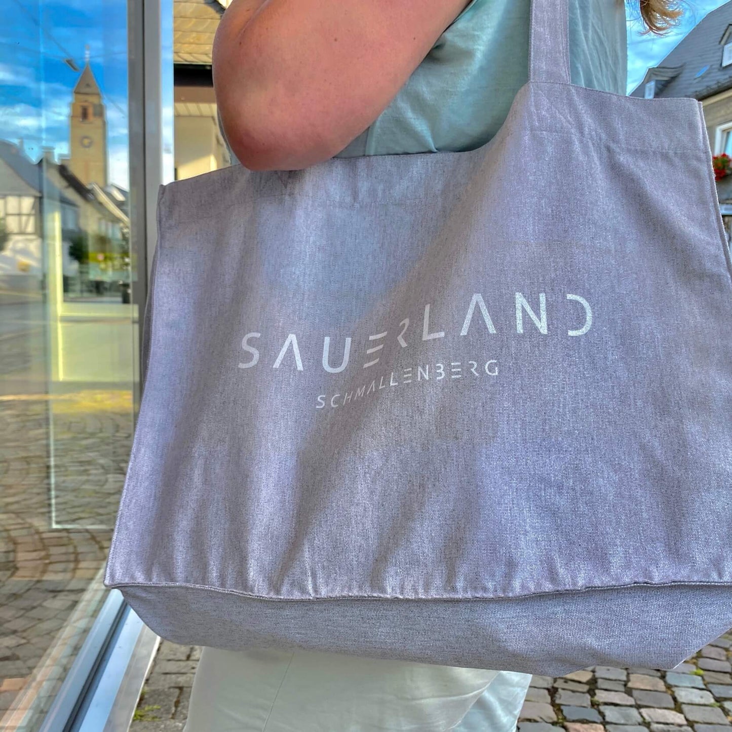 Einkaufstasche aus Baumwolle in hellgrau mit dem new SAUERLAND Schriftzug in weiß bedruckt. Darunter steht etwas kleiner in weiß der Stadtname Schmallenberg. Die Sauerland Dorftaschen können mit Deinem Wunschdorfnamen bedruckt werden.
