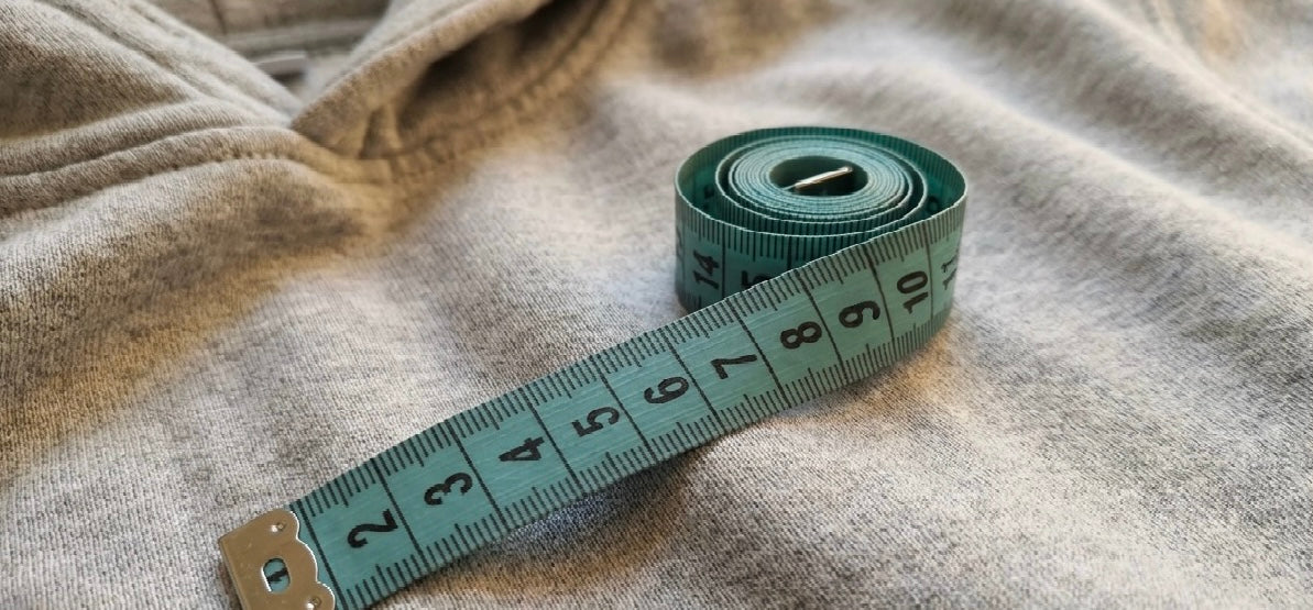 Ein türkises Maßband liegt auf einem grauen Hoodie