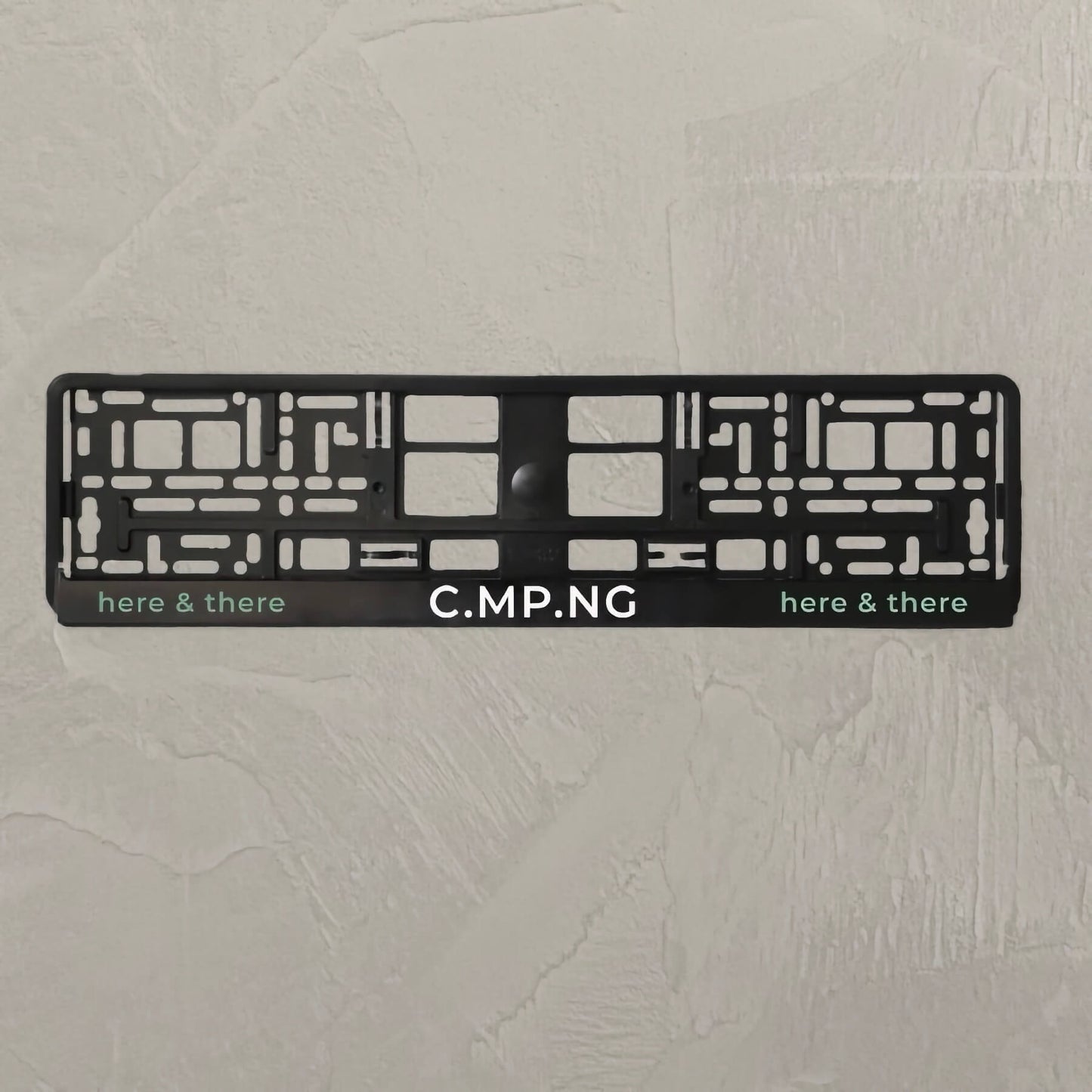Produktfoto des C.MP.NG Kenneichenhalter original.
In der Mitte steht C.MP.NG und rechts und links in grün „here & there“.