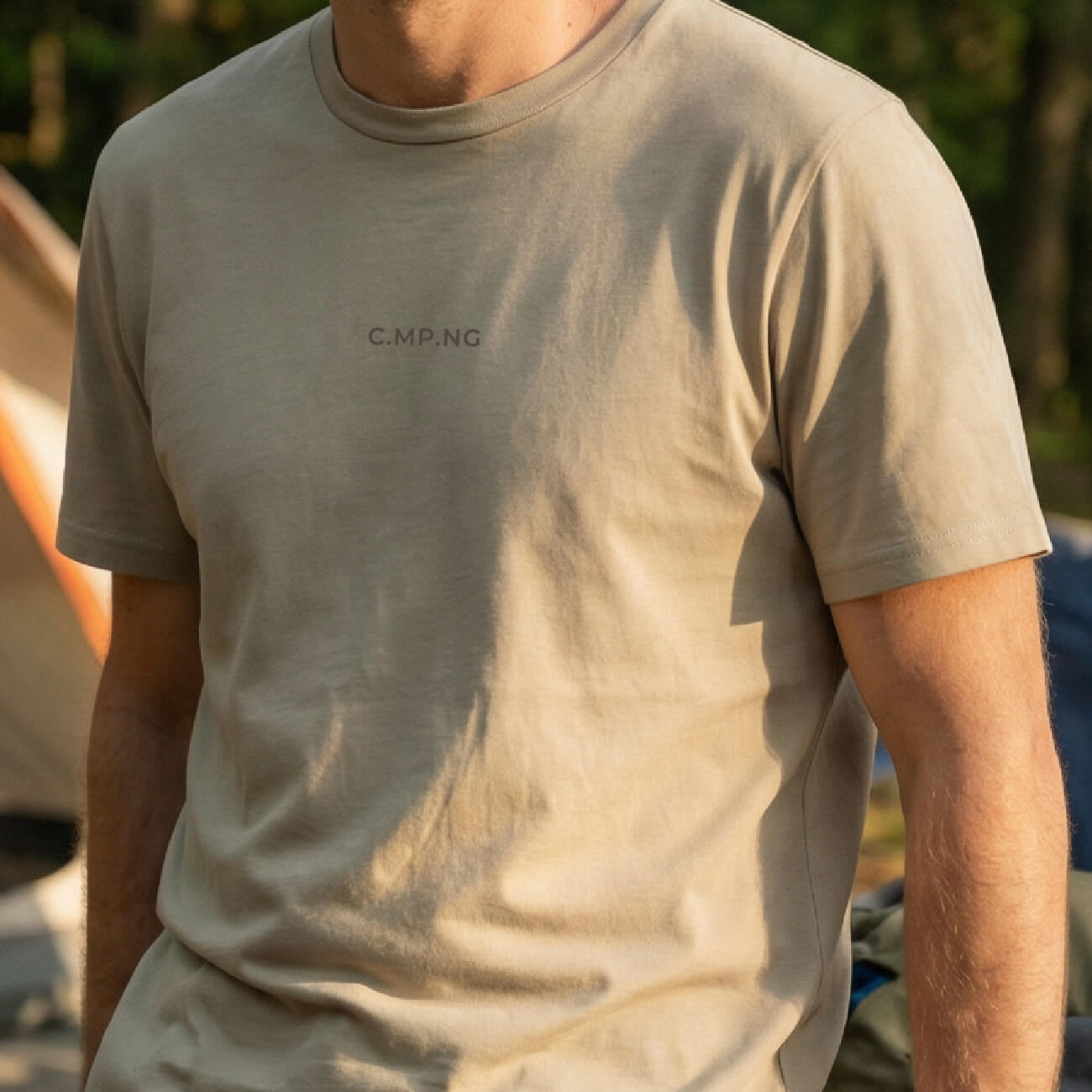 Mann trägt beiges C.MP.NG Basic T-Shirt beim Camping. Detail des dezenten C.MP.NG Logo-Prints auf der Brust.