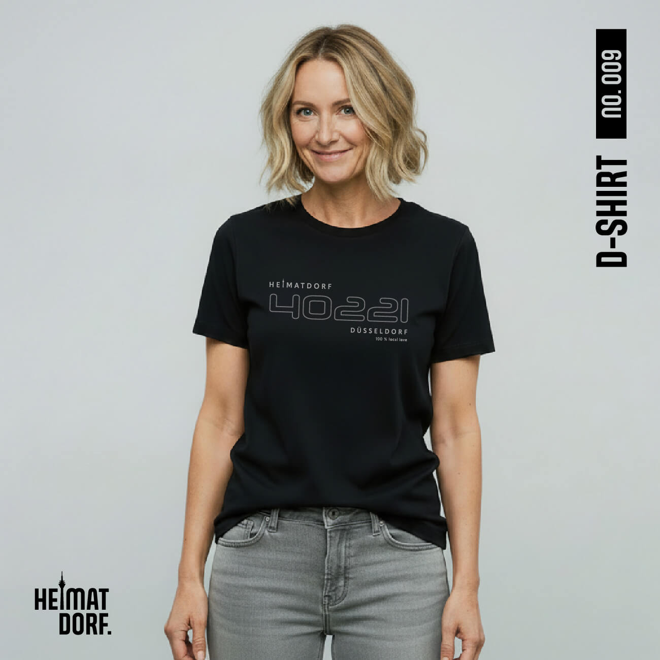 Frau trägt schwarzes, lässiges T-Shirt mit Düsseldorf Postleitzahl als Outline. Darüber befindet sich in hellgrau der Begriff HEIMATDORF, darunter Düsseldorf und 100 % Local Love.