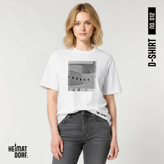 Junge Frau trägt weißes Düsseldorf T-Shirt zu einer grauen Jeans. Auf dem T-Shirt befindet sich in Graustufen ein Fotoausschnitt vom Düsseldorfer Schauspielhaus. Am unteren Rand ist der Begriff Heimatdorf in weiß aufgedruckt. Rechts oben ist ebenfalls in weiß "The white house" aufgedruckt. Das Düsseldorf T-Shirt ist die No. 012 der D-Shirt Kollektion.