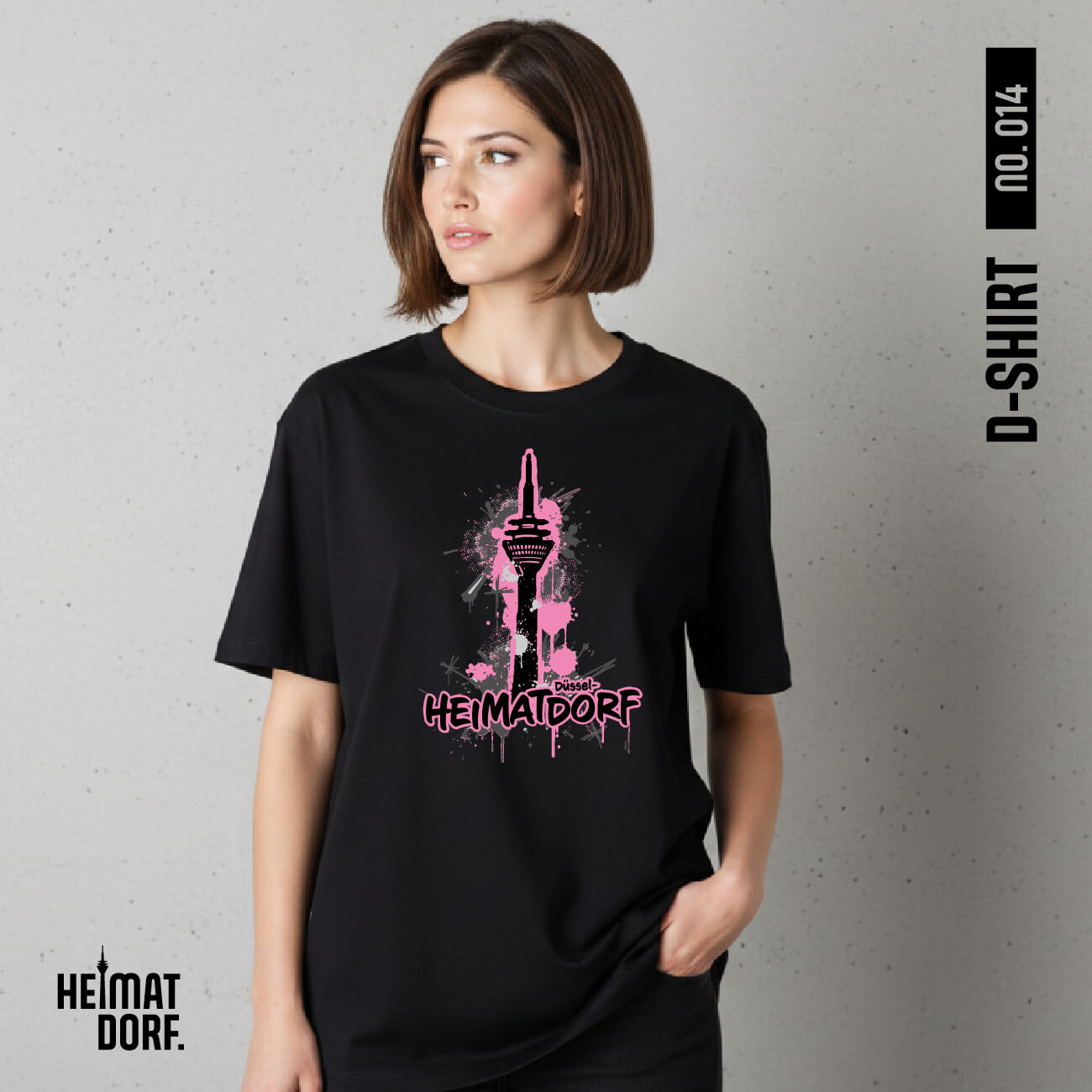 Brunette Frau trägt ein schwarzes, lockeres Düsseldorf T-Shirt mit Rheinturm und Schriftzug Heimatdorf Düsseldorf im urbanen Graffiti-Style. Der Aufdruck ist in schwarz-grau-Tönen gehalten mit Akzentfarbe Rosa.