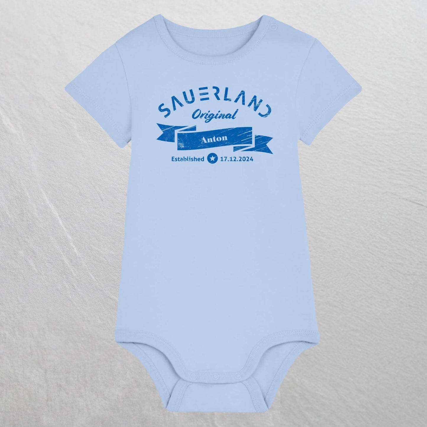 Hellblauer Baby-Body mit dunkelblauem Aufdruck Sauerland Original, dem Vornamen und Geburtsdatum des Babys.