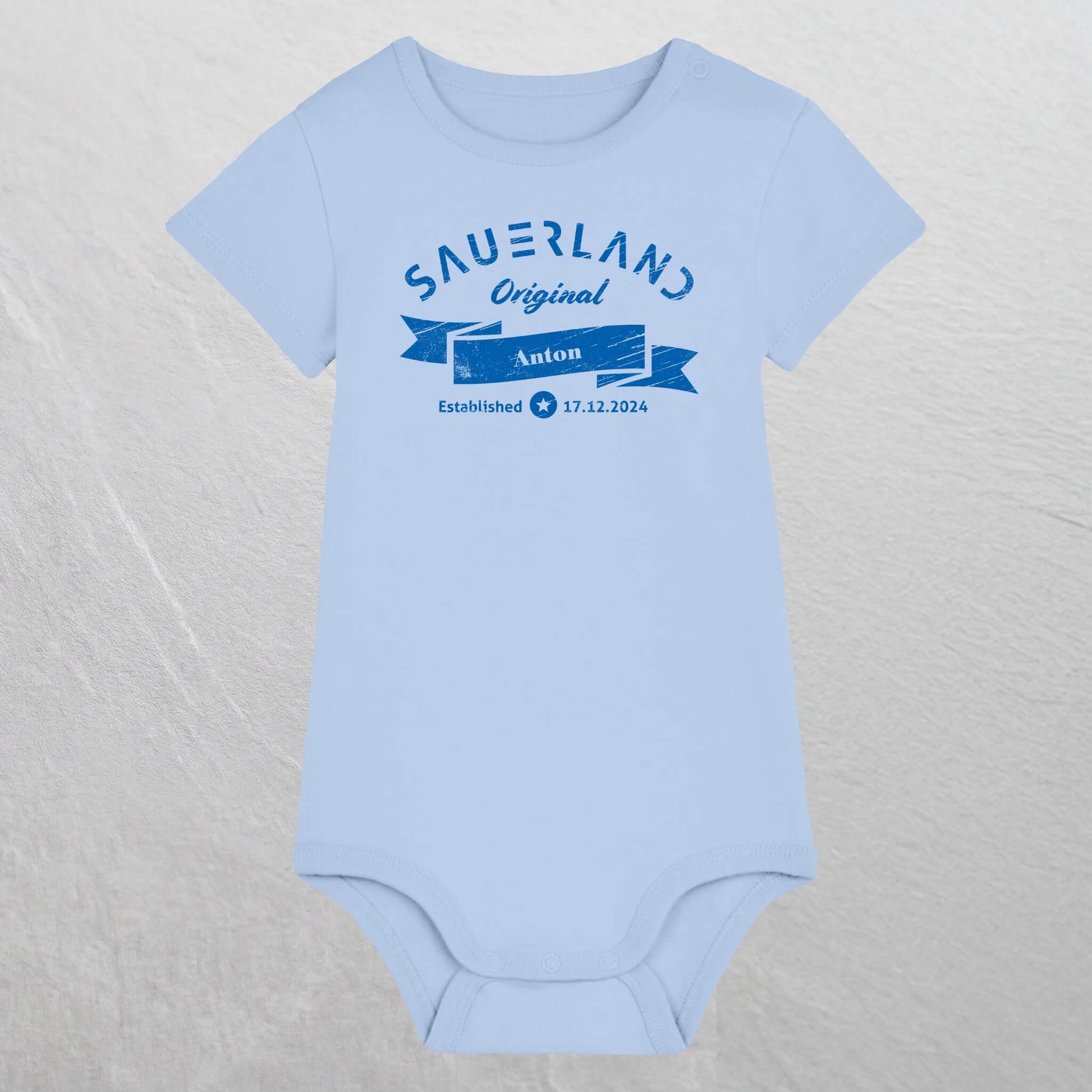 Hellblauer Baby-Body mit dunkelblauem Aufdruck Sauerland Original, dem Vornamen und Geburtsdatum des Babys.