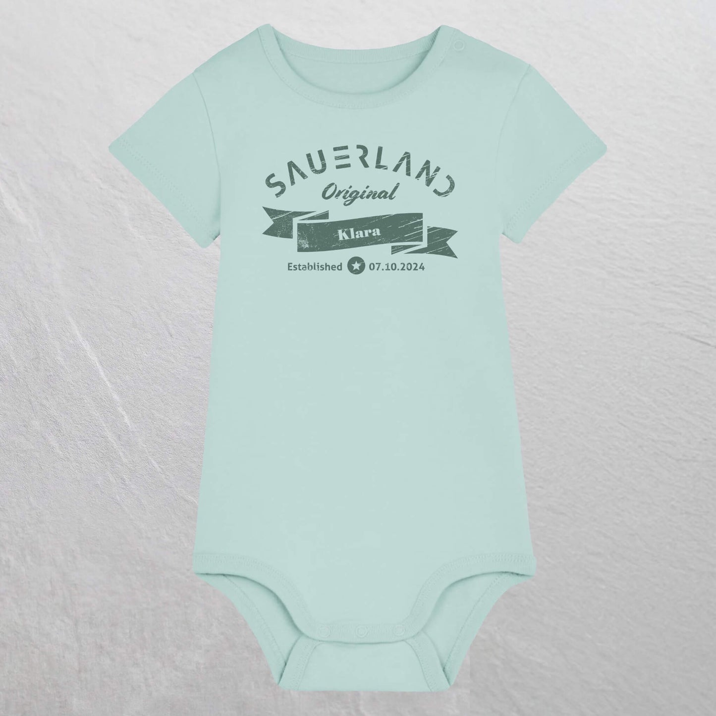 Karibikblau farbiger Baby-Body mit dunkelgruenem Aufdruck Sauerland Original, dem Vornamen und Geburtsdatum des Babys.