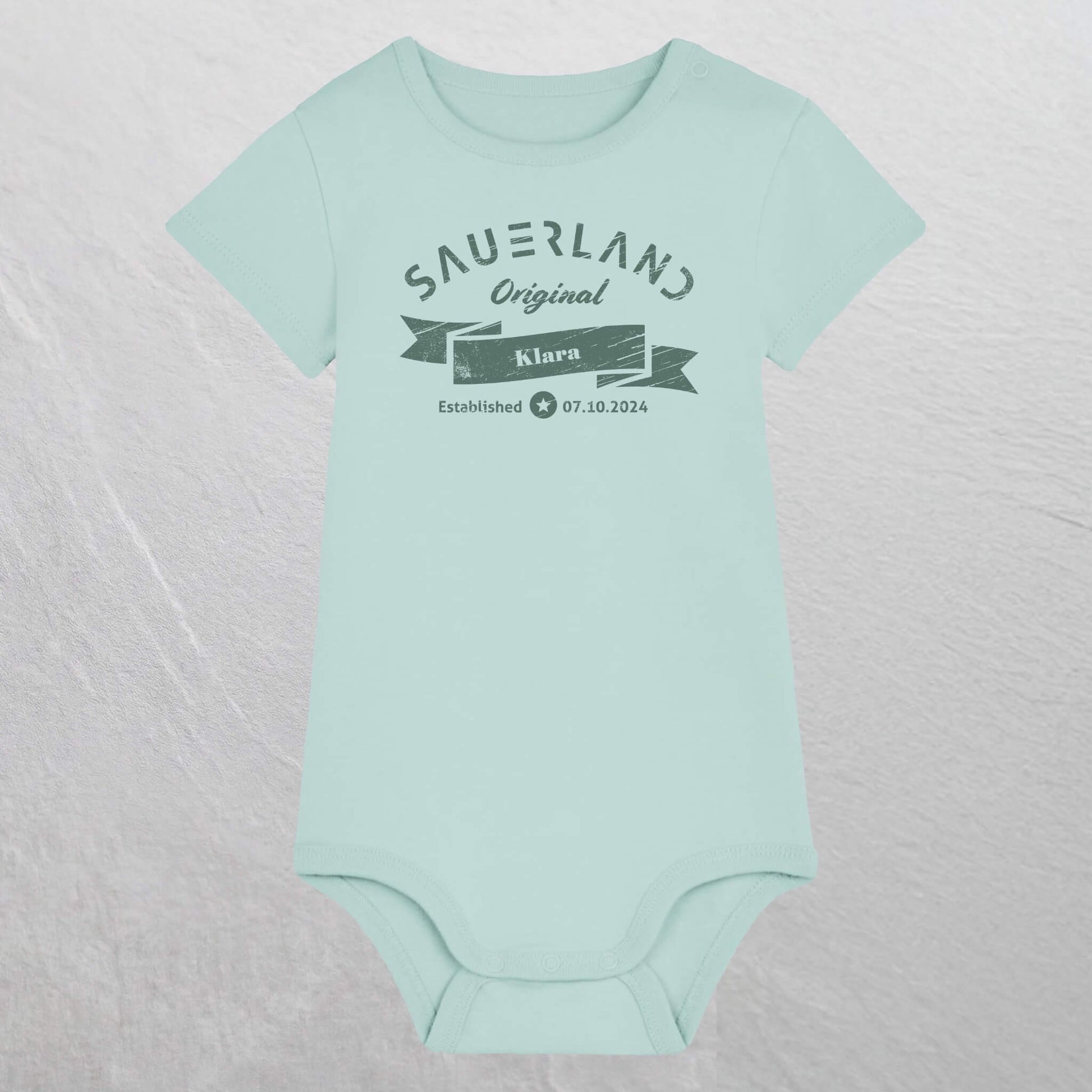 Karibikblau farbiger Baby-Body mit dunkelgruenem Aufdruck Sauerland Original, dem Vornamen und Geburtsdatum des Babys.