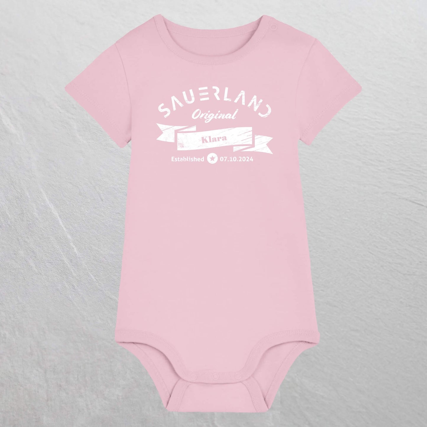 Rosa farbiger Baby-Body mit weißem Aufdruck Sauerland Original, dem Vornamen und Geburtsdatum des Babys.