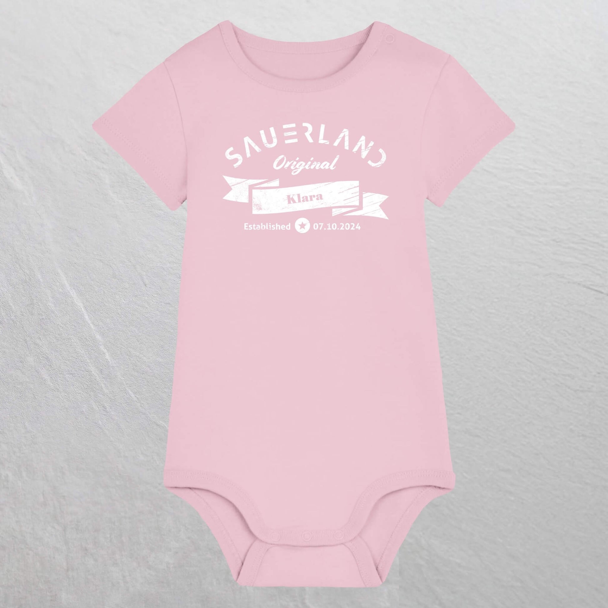 Rosa farbiger Baby-Body mit weißem Aufdruck Sauerland Original, dem Vornamen und Geburtsdatum des Babys.