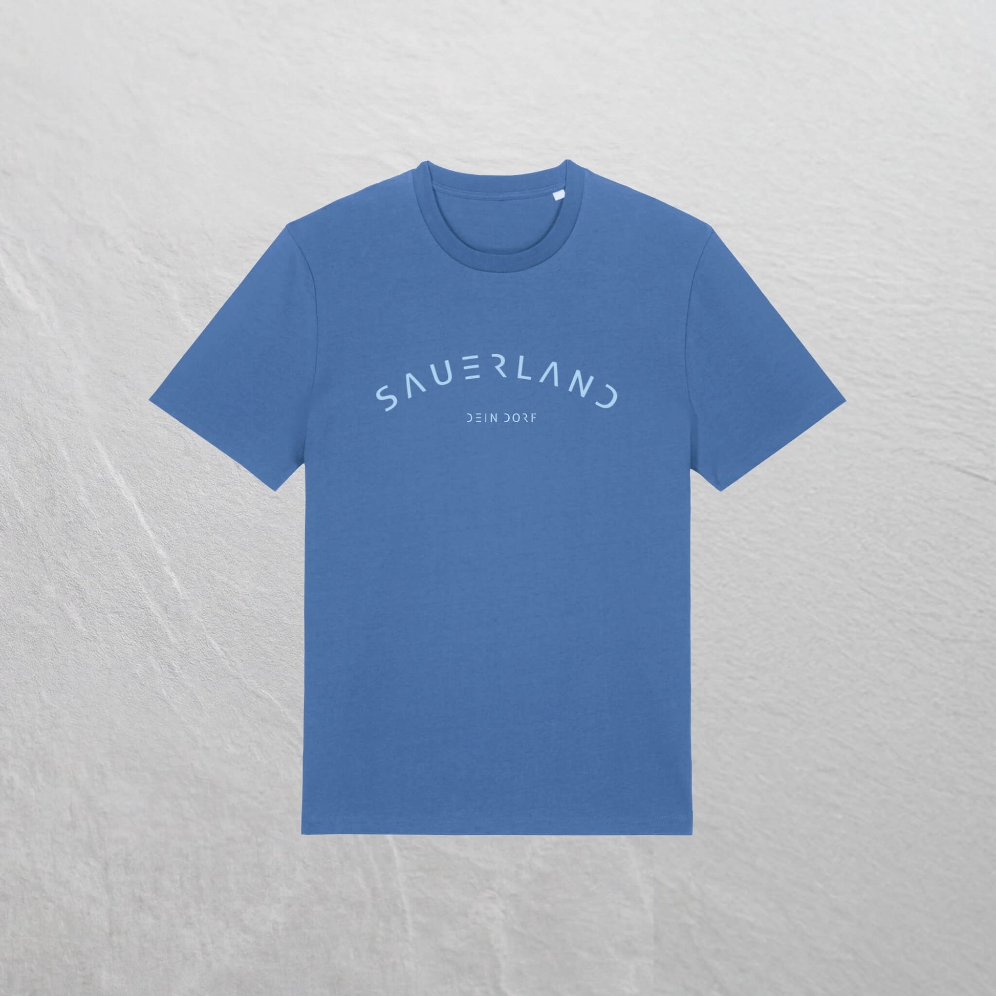 Mittelblaues T-Shirt mit leicht gerundetem Sauerland-Schriftzug liegt auf einem Holzhintergrund. In der Mitte unter dem Sauerland-Schriftzug ist der Dorfname Kierspe eingedruckt. Der Aufdruck ist hellblau.