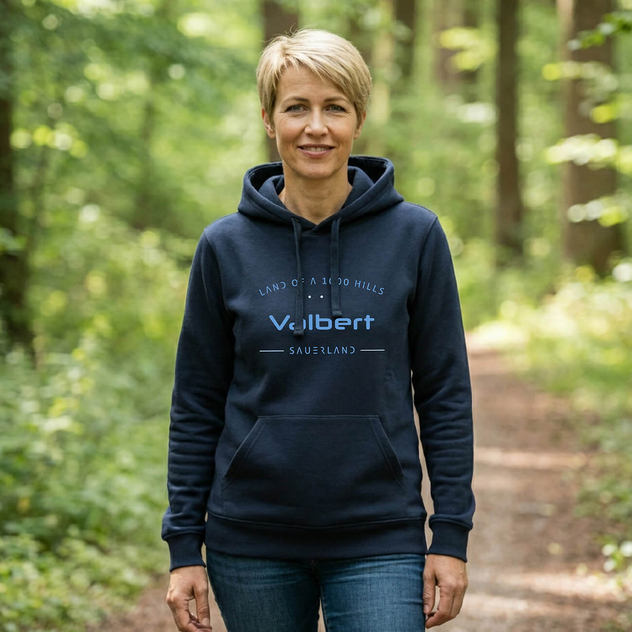 Eine Frau welche im Wald steht mit einem dunkelblauen Hoodie, Aufdruck des Hoodies ist: Land of a 1000 Hills - Valbert - Sauerland