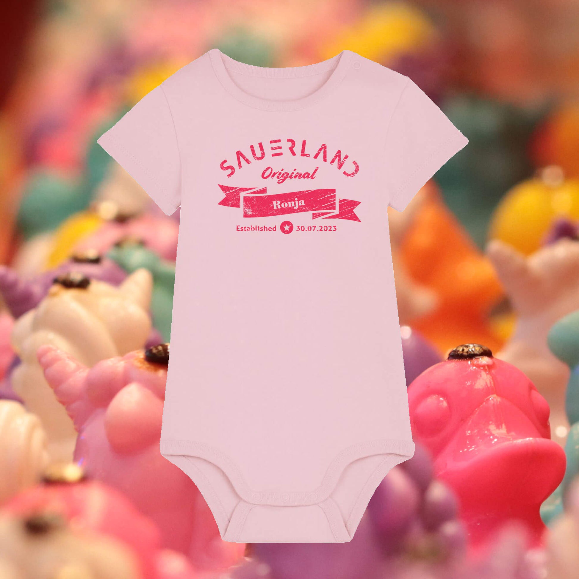 Rosa farbiger Baby-Body mit pinkfarbigem Aufdruck Sauerland Original, dem Vornamen und Geburtsdatum des Babys.