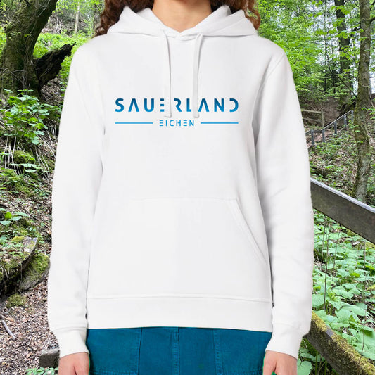 Frau in weißem Hoodie aus Biobaumwolle mit in einem blau-hellblau verlaufenden Aufdruck Sauerland Eichen steht auf einem Weg im Wald