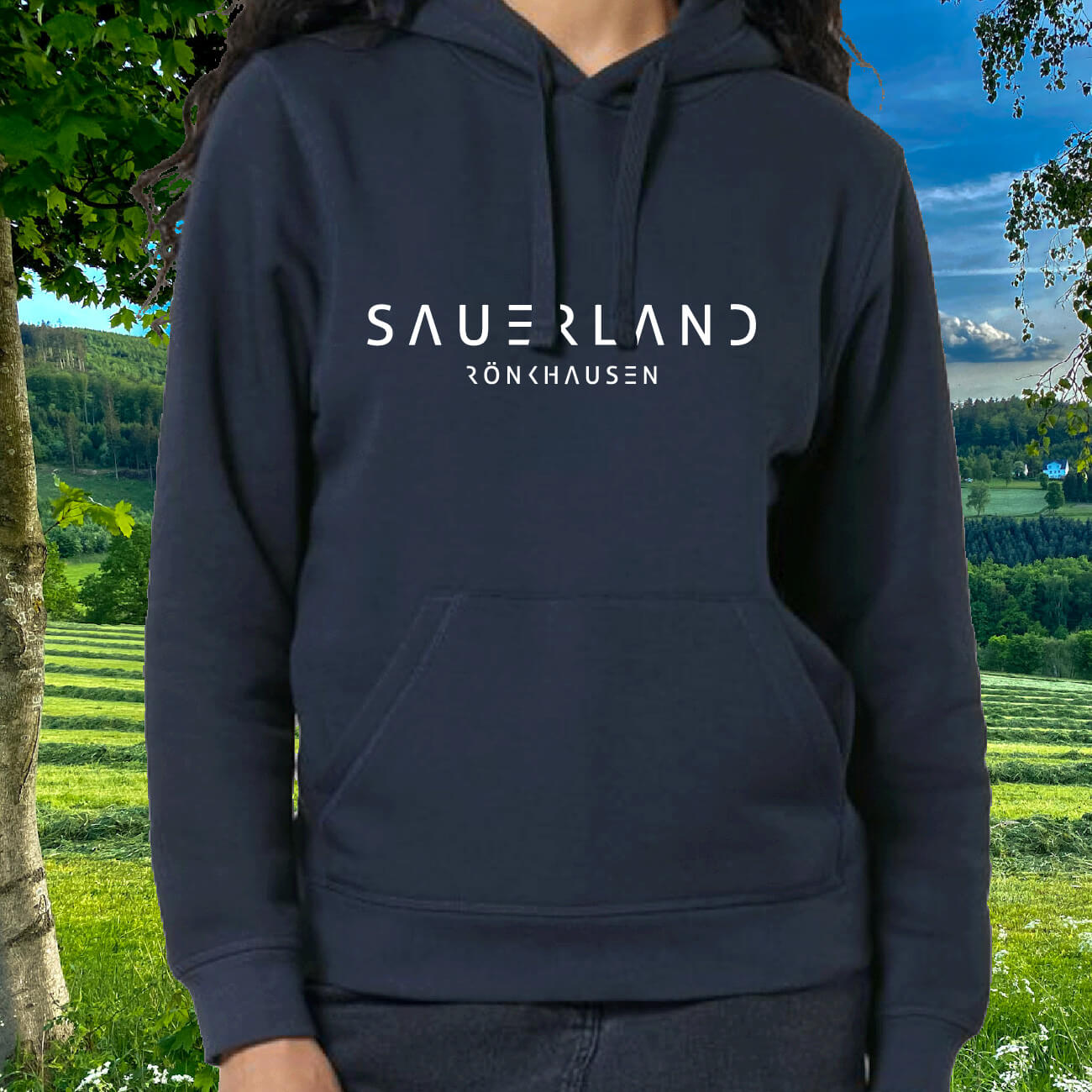 Frau in dunkelblauem Bio-Hoodie mit weißem Aufdruck Sauerland Rönkhausen steht inmitten der Sauerländer Natur