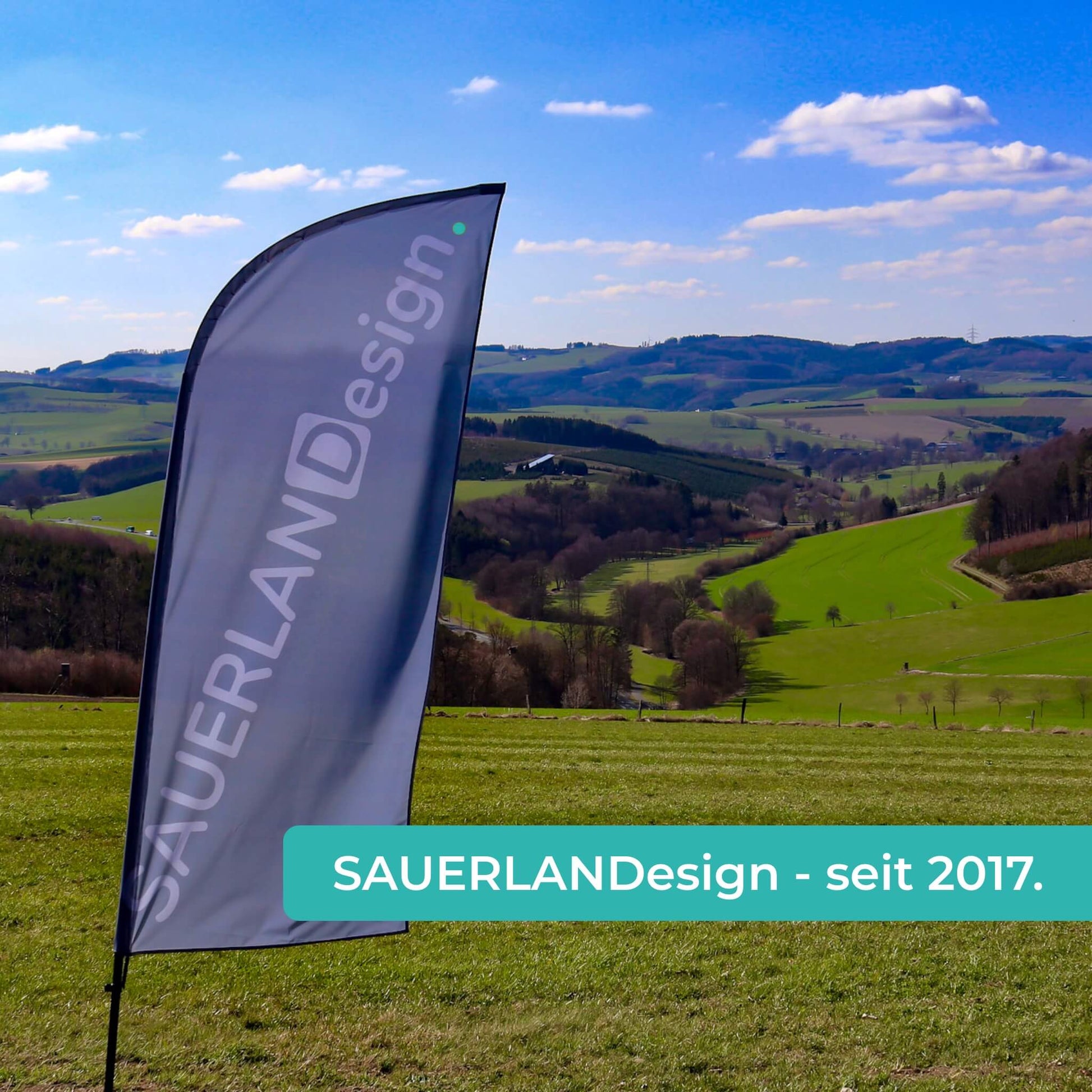 Eine Fahne von SAUERLANDesign ist in der sauerländer Natur. Der Text: SAUERLANDesign - seit 2017 ist lesbar