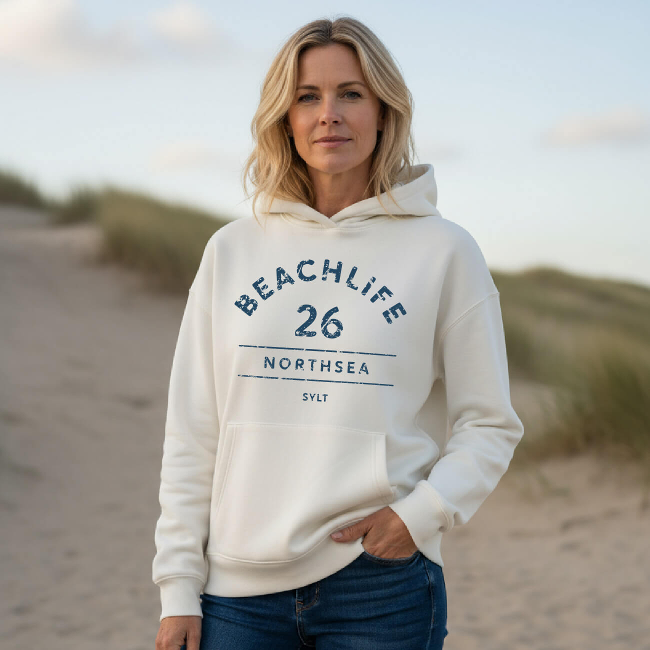BEACHLIFE 26 Sylt Hoodie in Vanille. Frau trägt Bio-Baumwoll Hoodie mit Frontprint am Strand