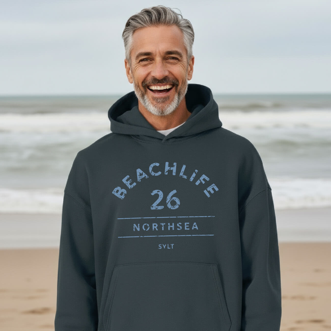 Mann trägt unisex Sylt-Hoodie BEACHLIFE 26 in grau-blau mit Used-Look Print in Jeans-Blau - Relaxed Fit Frontansicht