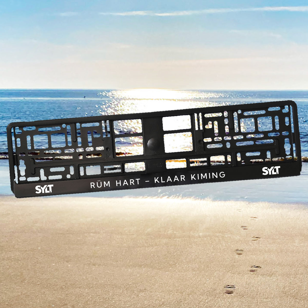 Sylt Kennzeichenhalter mit modernem Sylt-Schriftzug links und rechts. In der Mitte steht der friesische Spruch "Rüm hart – Klaar Kiming". Im Hintergrund des Nummernschildhalters sieht man die Sylter Nordsee mit Spiegelung des Sonnenscheins.