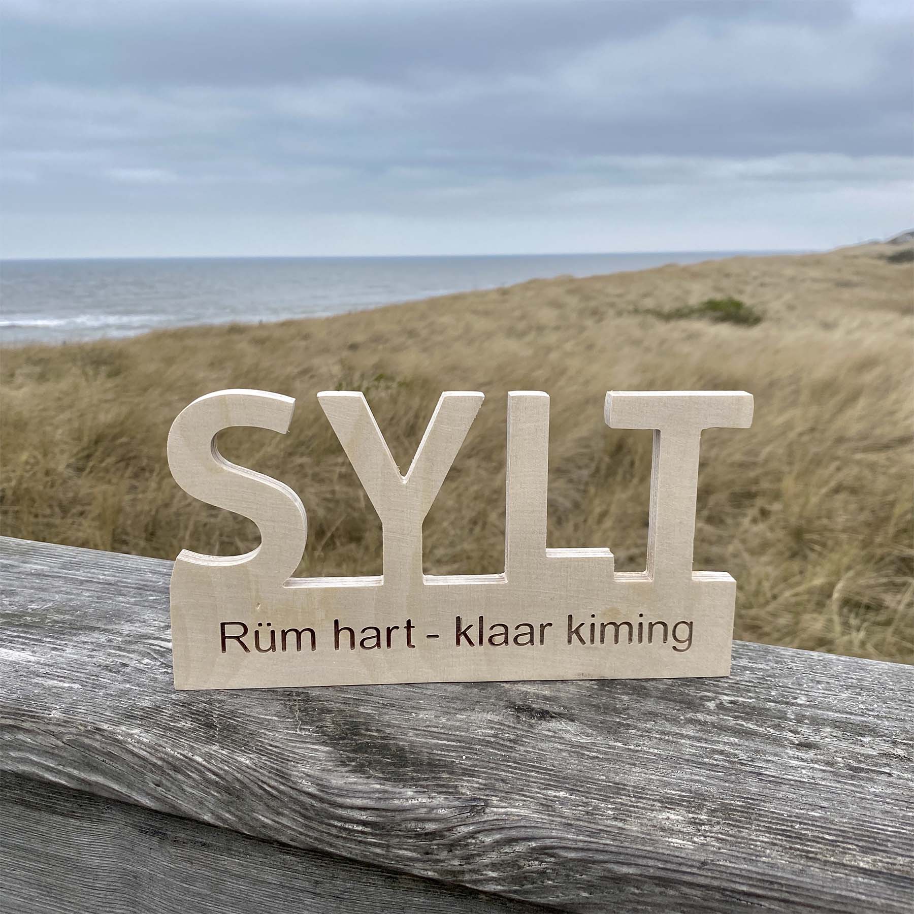 Holz Deko-Schild mit dem Begriff Sylt Rüm hart klar kiming steht am Strandausfgang mit Blick in die Dünen und aufs Meer.
