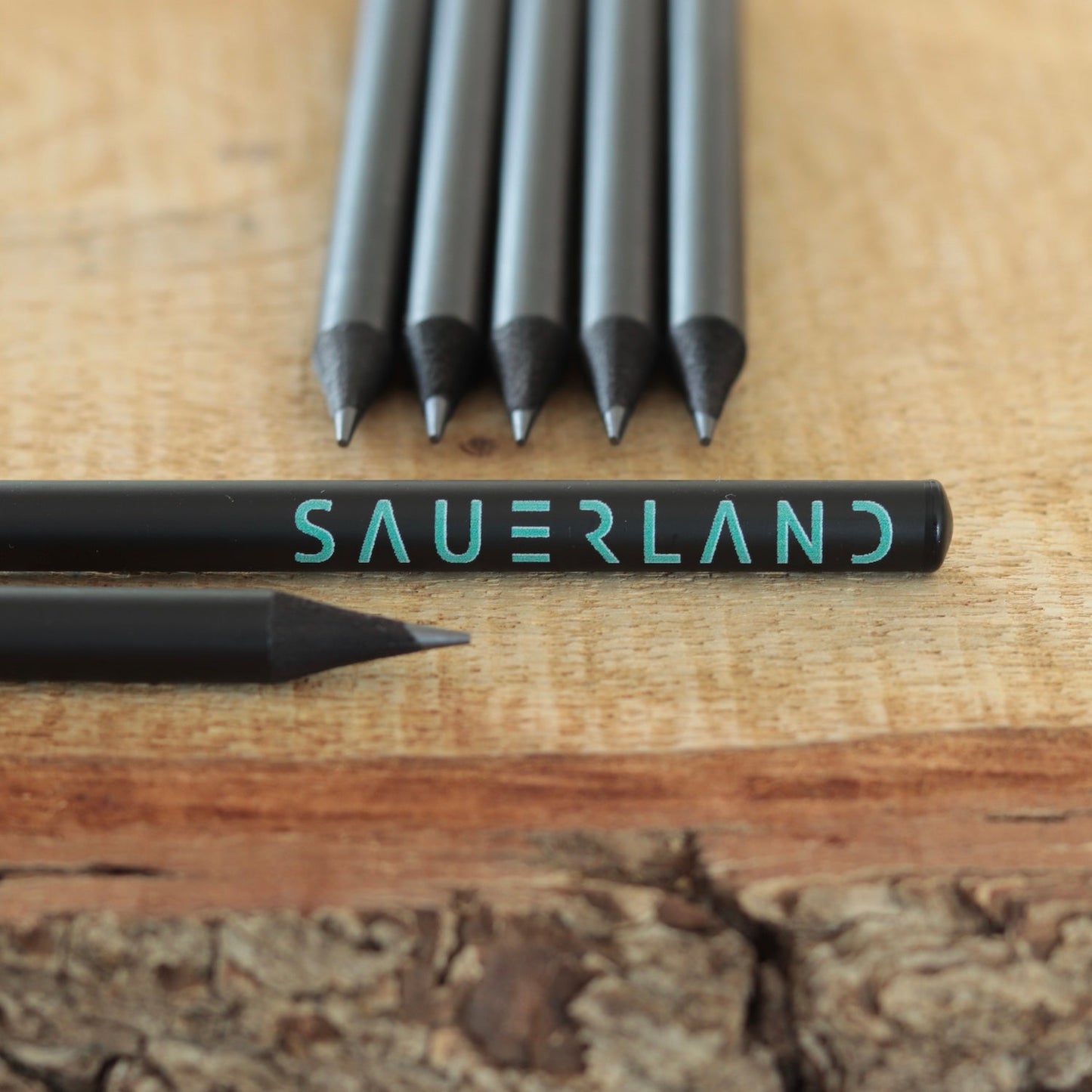 Schwarze Sauerland Bleistifte mit dem New Sauerland Schriftzug in türkis. Die Bleistifte sind matt-schwarz und haben eine schwarze Tauchkappe am Ende.