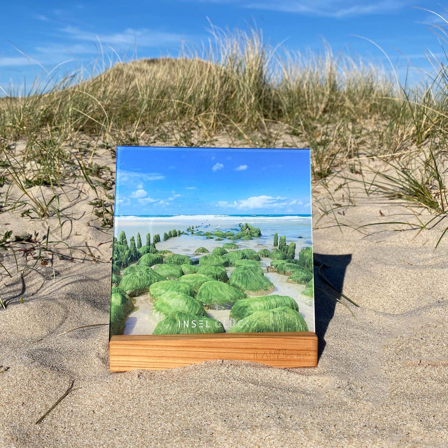 Acrylbild mit vermoosten Buhnenresten in der tosenden Sylter Nordsee steht in einem Holzbilderhalter. Das Set steht in den Sylter Dünen.  