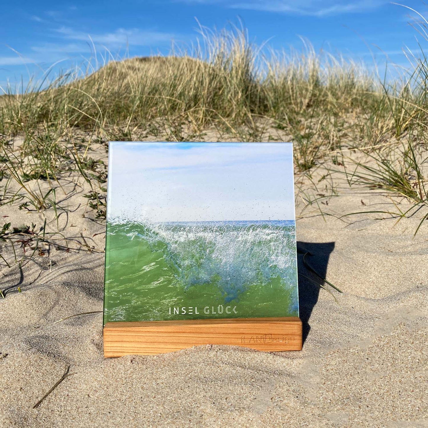 Acrylbild mit einer sich gerade brechenden Welle steht in einem Standbilderhalter aus Holz in den Sylter Dünen.
